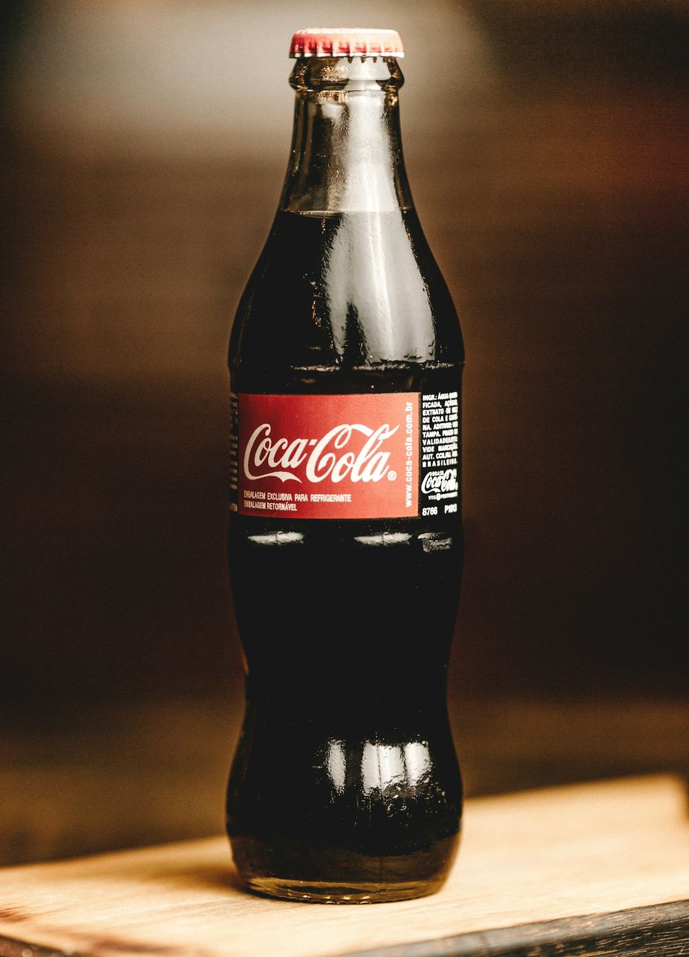 A glass Coca-Cola contour bottle on a wooden board