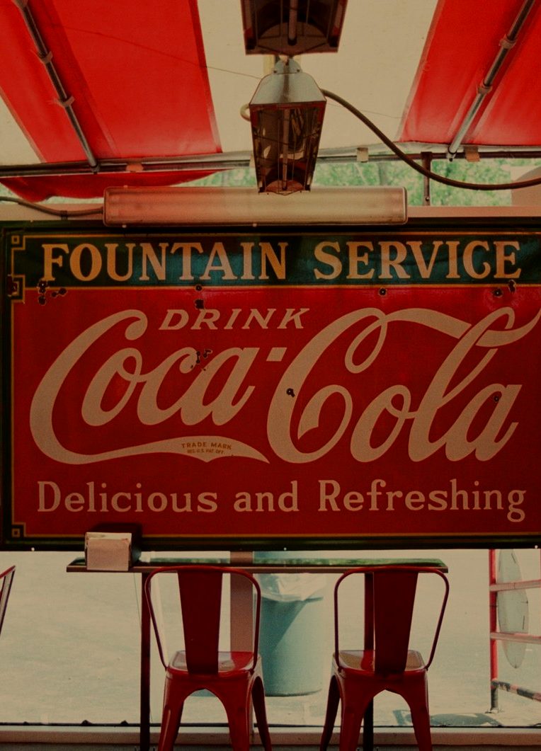 A Fountain Service Drink Coca-Cola sign above red chairs