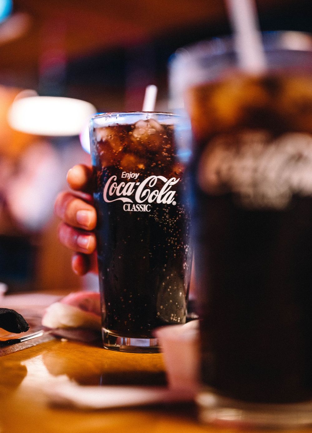 A hand holding a glass of Coca-Cola with ice